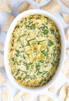 spinach and artichoke dip in a white bowl surrounded by crackers