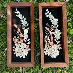 two framed pictures with flowers and leaves on them sitting in the grass next to each other