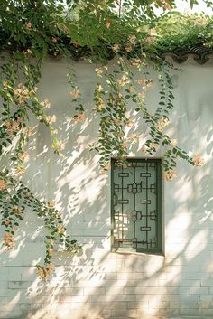 an open window on the side of a white brick building with vines growing over it