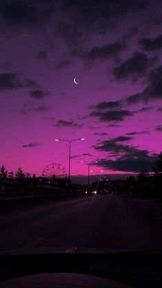 the night sky is purple and pink with some clouds in it, as seen from an empty street