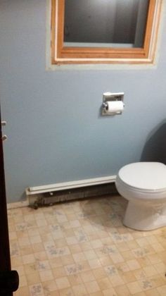 a white toilet sitting in a bathroom next to a window with a wooden frame above it