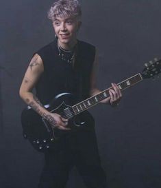 a man with pink hair is holding a guitar and posing for a photo in front of a black background