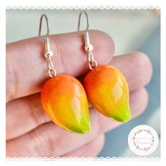 two oranges with green leaves are hanging from silver earwires on a white background