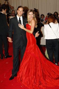 a man and woman in formal wear standing on a red carpet with cameras around them