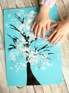 a child's hand is touching a tree painted on a piece of blue paper