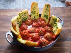 a pan filled with meatballs and bread on top of a wooden table next to a knife