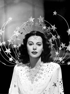 a woman with stars on her head wearing a white dress and gold necklaces,