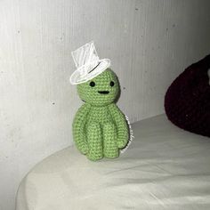 a crocheted green stuffed animal with a white hat on it's head