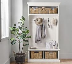 a white coat rack with baskets and hats on it next to a potted plant