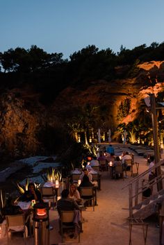 people are sitting at tables on the beach in front of an ocean side restaurant with candles lit up