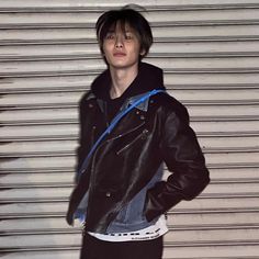 a young man standing in front of a garage door wearing a leather jacket and jeans