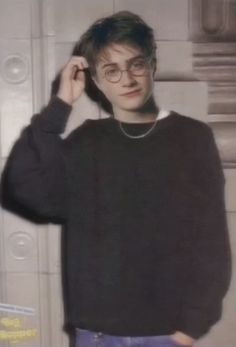 a young man wearing glasses and a black sweater standing in front of a white wall