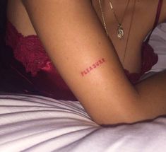 a woman with a tattoo on her arm that says pleasure in red ink sitting on a bed