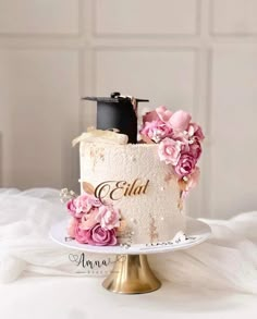 a wedding cake decorated with pink flowers on a white tablecloth and gold plated stand