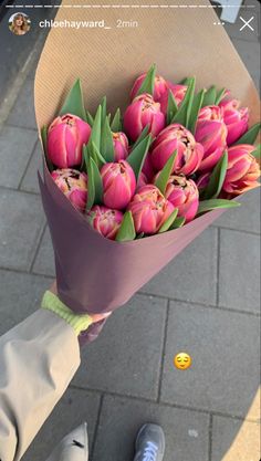 a person holding a bouquet of pink tulips in their hand on the sidewalk