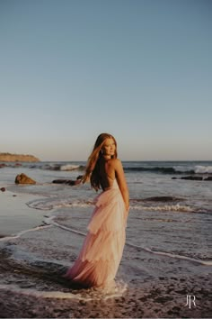 a woman in a pink dress standing on the beach