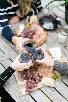 two people toasting wine glasses over grapes on a wooden table