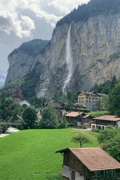 a small village sits in front of a large mountain with a waterfall coming out of it