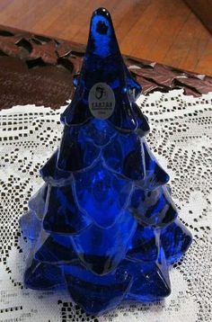 a blue glass christmas tree sitting on top of a doily covered table with lace