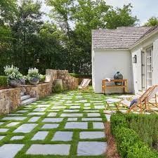 an outdoor patio with grass and stepping stones in the ground, next to a small white house