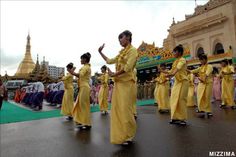 a group of people in yellow dresses are dancing on the street with their hands together