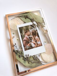 a photo frame with flowers and greenery on the inside is surrounded by leaves, twigs, and branches