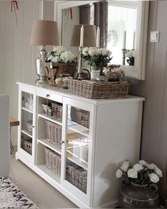 a white dresser with baskets on top and flowers in vases sitting next to it