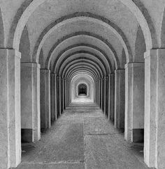 black and white photograph of a long tunnel with columns on both sides, leading into the center