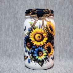 a painted mason jar with sunflowers and butterflies on the lid, tied to a string