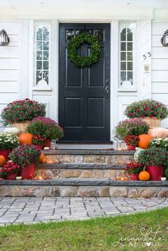 front porch decorated for fall with pumpkins and flowers on the steps next to the door