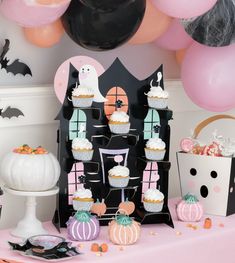 a table topped with cupcakes and cake next to halloween decorations in front of balloons