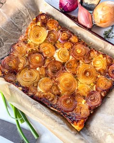 there is a square pastry with onions on the table next to garlic and other vegetables