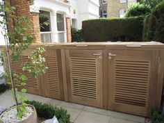 a wooden outdoor storage unit with shutters on the doors and side panels, in front of a house