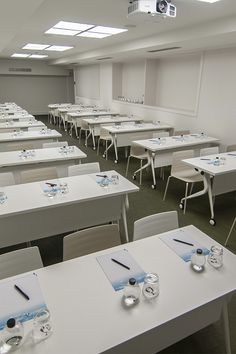 an empty classroom with white desks and blue place mats on the desks are lined up in rows