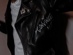 a person wearing a black leather jacket with white writing on the side and zippers