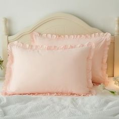 two pink pillows on top of a white bed next to a night stand with flowers