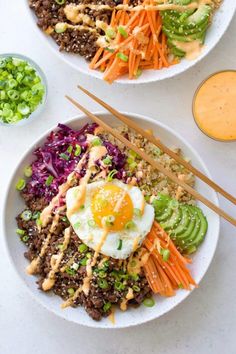 two white bowls filled with rice, carrots and an egg sitting on top of each other