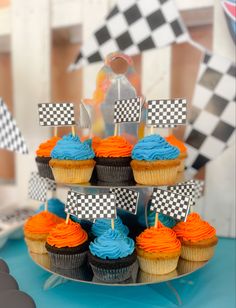 cupcakes with blue and orange frosting are on a cake stand in front of a race flag