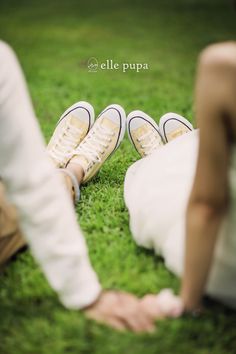 two people sitting in the grass with their feet on each other's legs and one person wearing white shoes