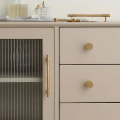 a white dresser with gold handles and knobs next to a bottle on top of it