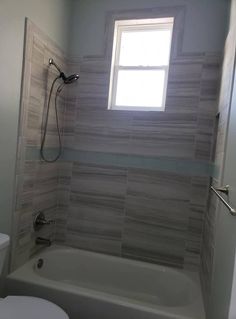 a white toilet sitting under a window next to a bath tub