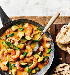 a pan filled with shrimp and vegetables next to pita bread