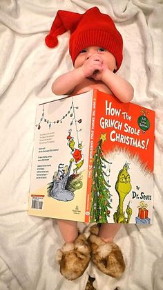 a baby laying in bed with a book about how the grinch stole christmas by dr seuss