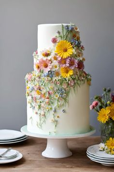 a white cake with flowers on it sitting on top of a table next to plates