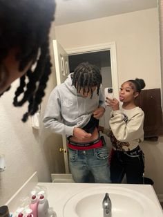 two people standing in front of a bathroom mirror looking at their cell phones and taking pictures