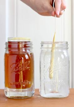 a person is pouring honey into a mason jar with a wooden spoon and another hand holding a stick