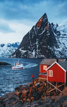 a boat is in the water next to some red buildings and snow - capped mountains