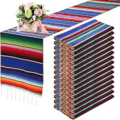 a stack of multicolored table cloths next to a vase with flowers on it