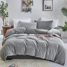 a bed with grey sheets and pillows in a room next to a potted plant