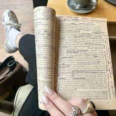 a woman is holding an open book with writing on it in her left hand while sitting at a table